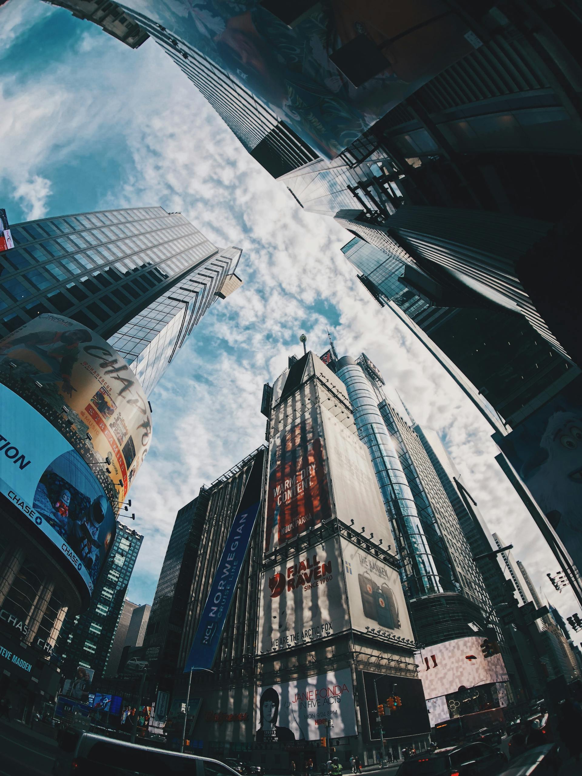 A striking fisheye view of skyscrapers under a bright sky in Times Square, NYC.